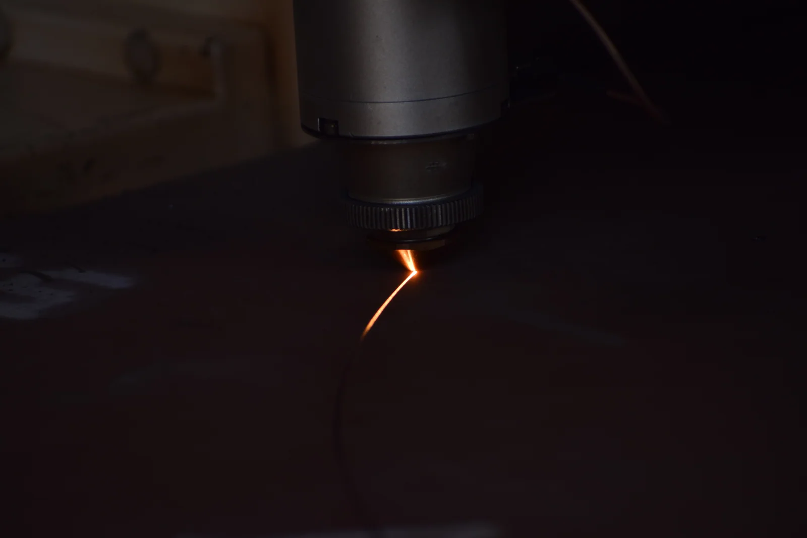 Laser cutting head piercing sheet metal in the dark, with sparks flying